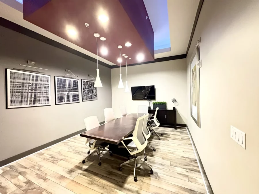 community conference room with seating for eight at a large table, pendant lighting, and a TV mounted on the wall.