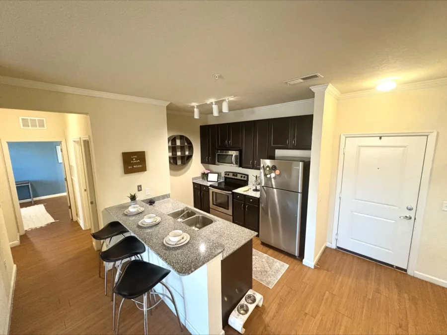 apartment kitchen with chocolate brown cabinets, stainless appliances, and a large island with bar seating, sink and granite countertops.