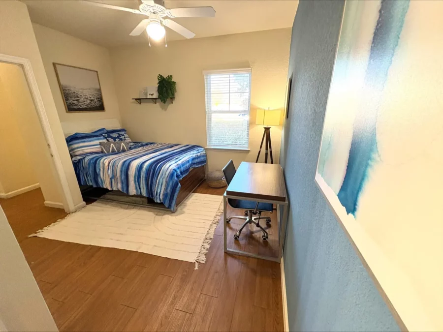 apartment bedroom with wood style flooring, a tall bed with storage underneath, a desk, and large window