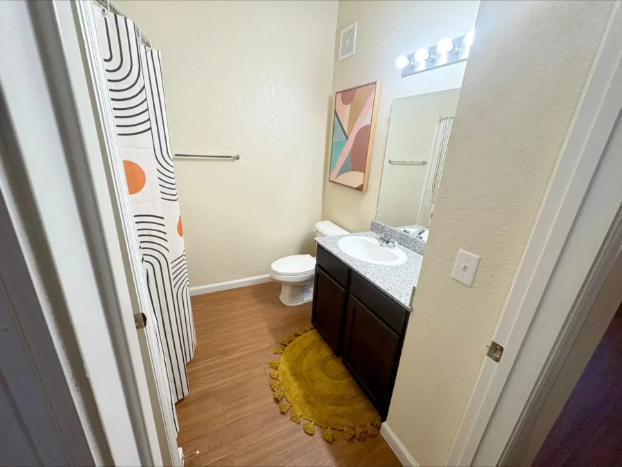 apartment bathroom with curved shower rod, wood style flooring, and single vanity with granite countertop