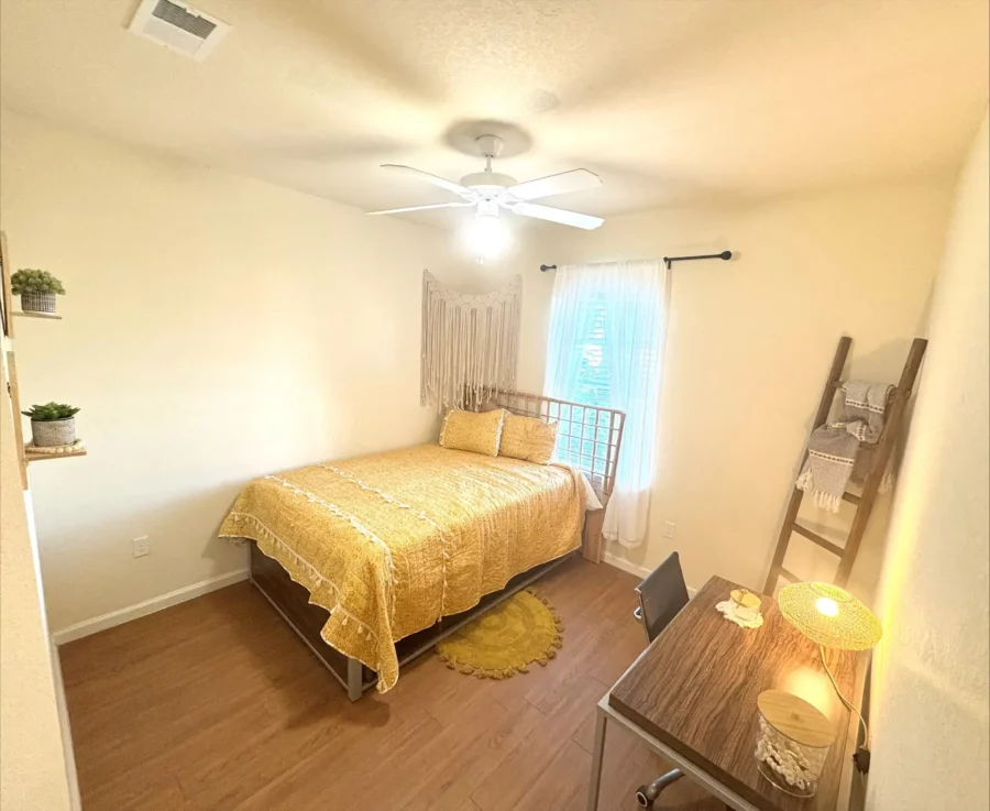 apartment bedroom decorated in boho style with wood style flooring, a tall bed with storage underneath, a desk, and large window