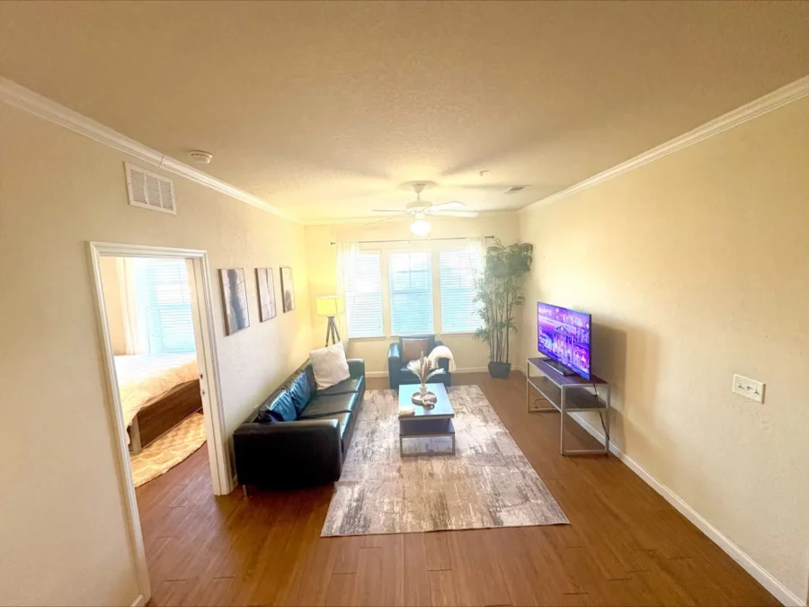 apartment living room with three windows, wood style flooring, a couch plus loveseat, coffee table, and TV