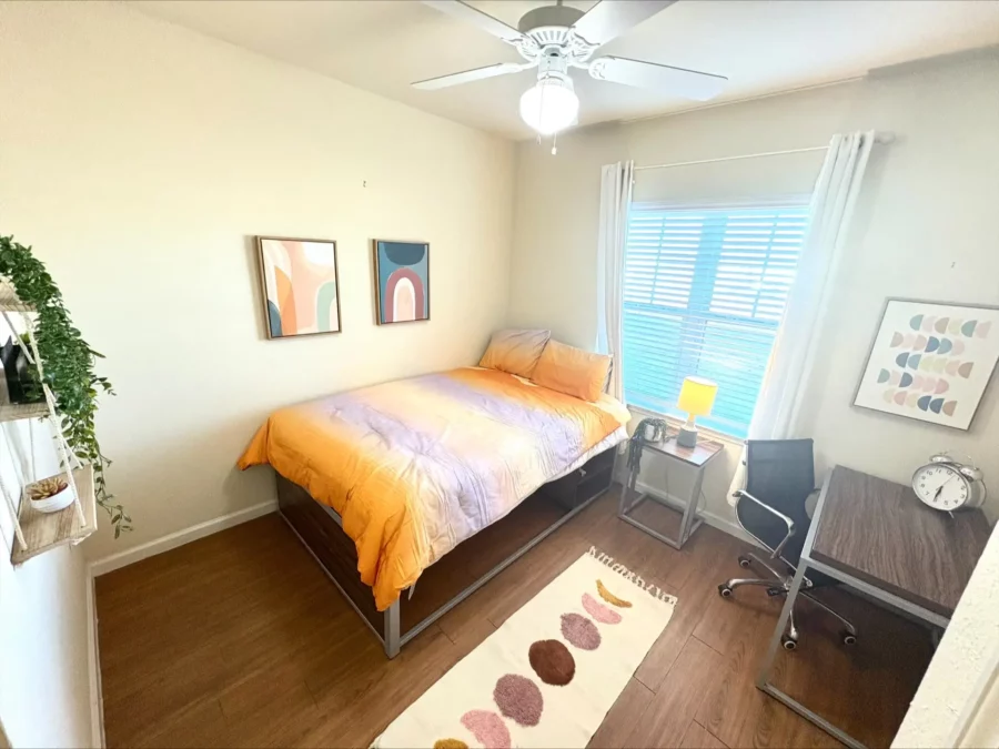 apartment bedroom with wood style flooring, a tall bed with storage underneath, a desk, and large window