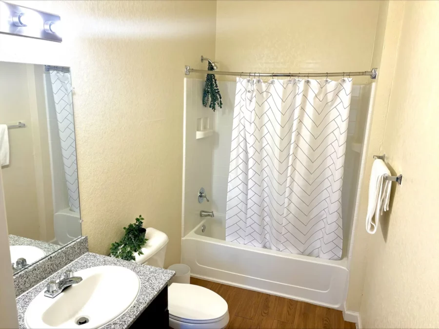 apartment bathroom with curved shower rod, wood style flooring, and single vanity with granite countertop