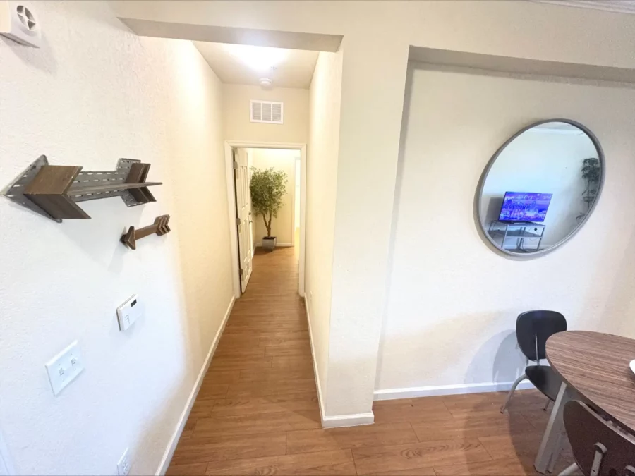 apartment hallway with wood style flooring leading from dining room to bedroom with an artificial potted tree.